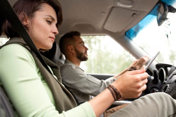 Woman in passenger seat looking at her phone while a man drives the car