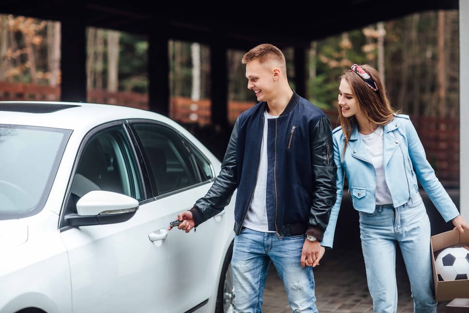 Young couple smiling while unlocking their white car outside their home