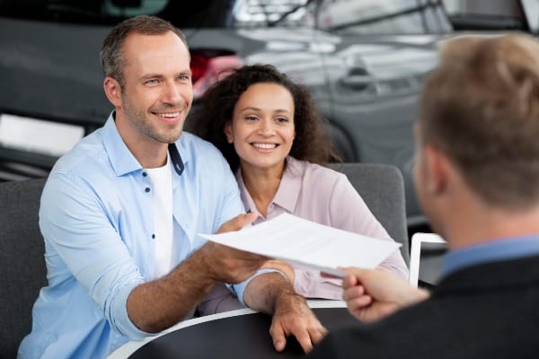 Smiling couple sitting at a desk while negotiate better auto insurance rates with their agent 