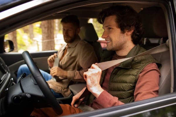Two men sitting in a car, fastening their seat belts before starting to drive
